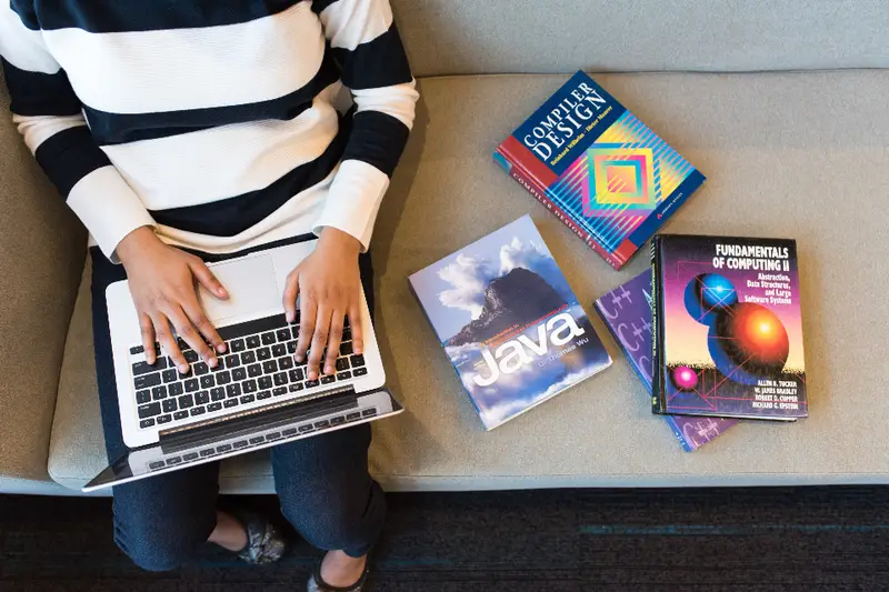 Persona con un portátil y varios libros de programación