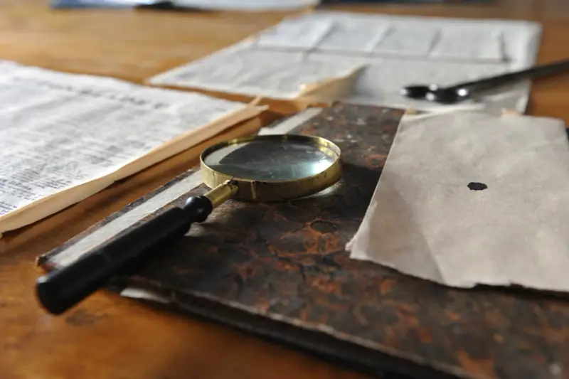 Documentos con anotaciones sobre una mesa junto a una lupa