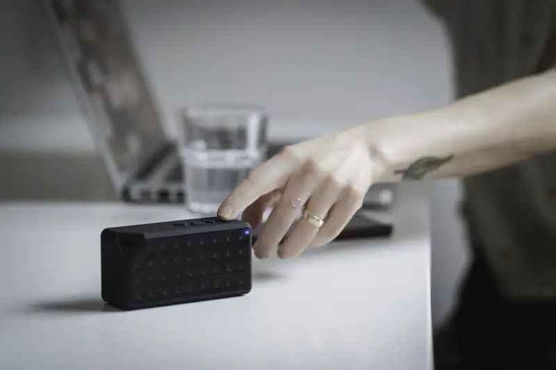 Mano encendiendo un altavoz Bluetooth sobre una mesa