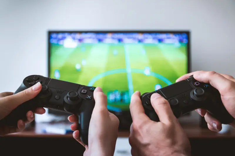 Dos mandos de consola jugando a la vez frente a la pantalla